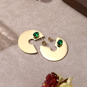 Dettaglio di orecchini dorati a C con una pietra preziosa verde incastonata