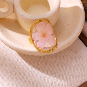 Detail of light pink dried flower preserved in resin inside a gold oval frame ring