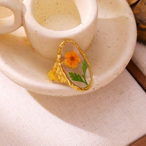 Close-up of golden stainless steel ring with orange dried flower specimen and hammered texture