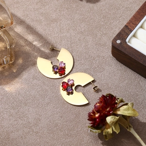 Dettaglio di orecchino a C dorato con pietre preziose a cuore rosa rosse e viola