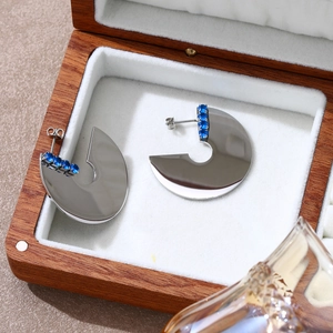 Dettaglio degli orecchini geometrici in argento con zirconi blu in una scatola portagioie in legno