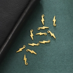 Gros plan de pendentifs éclair en acier doré sur fond vert texturé pour création bijoux