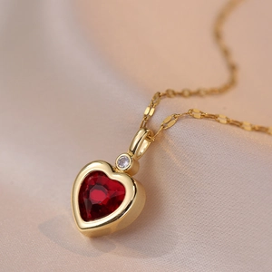 Close-up of a gold necklace with a faceted heart-shaped red zircon pendant on silk fabric