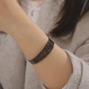 Black stainless steel open bangle with Celtic knot cutout design on model's wrist