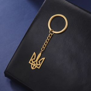 Golden stainless steel Ukraine Tryzub coat of arms keychain on a black leather background