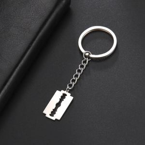 Close-up of a stainless steel razor blade pendant keychain on black leather surface