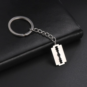 Close-up of polished stainless steel razor blade pendant keychain on black leather surface