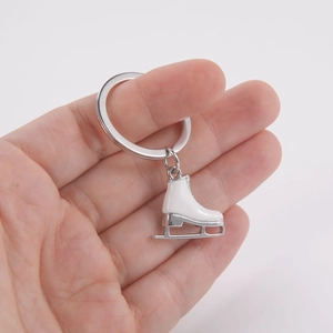 Porte-clés patin à glace avec pendentif en émail blanc et lame argentée tenu en main