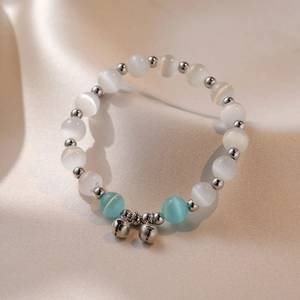 Detailopname van kralenarmband met kattenoogsteen en zilveren bellen op zijde