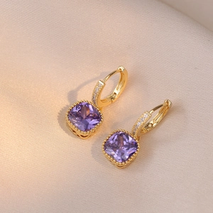 Vue macro de boucles d'oreilles dorées avec cristaux violets carrés et zircons