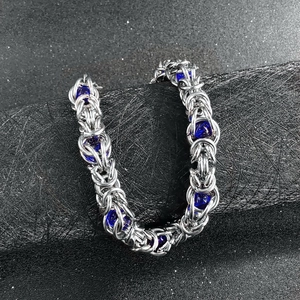 Detailed close-up of handmade steel chain bracelet with deep blue beads on black pedestal
