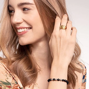 Detailaufnahme eines strukturierten Goldrings und schwarzen Perlenarmbands an einem Model