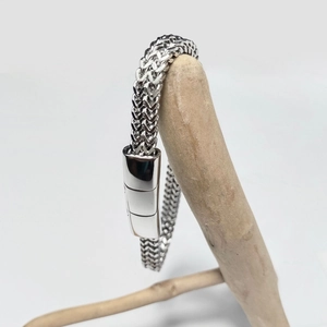 Detail of silver stainless steel wheat chain bracelet with magnetic clasp on wood branch