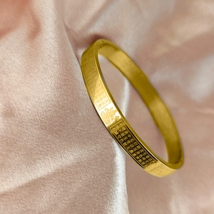 Detail shot of golden Buddhist Heart Sutra bracelet with etched scriptures and Buddha relief