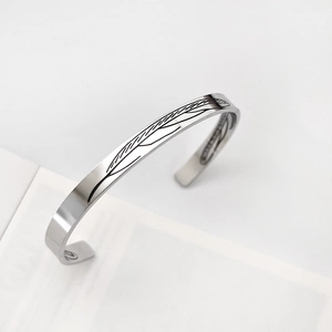 Vista dettagliata del bracciale rigido argento con incisione di piume e design aperto