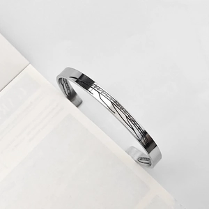 Dettaglio macro della trama piumata in argento sul bracciale aperto minimalista da uomo