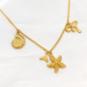 Detailansicht goldener Meeresanhänger mit Seestern, Muschel und Fischschwanz an einer Halskette