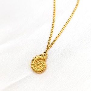 Nahaufnahme des goldenen Nautilus-Anhängers an feiner Kette auf weißem Stoff