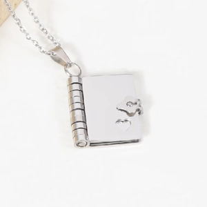 Close-up of a silver book locket pendant with heart cutout and textured spine details