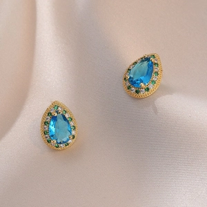 Elegantes pendientes de gota con circón azul y halo brillante sobre seda suave