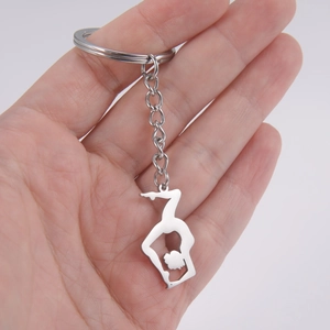 Gymnast silhouette keychain in polished stainless steel held in palm for scale
