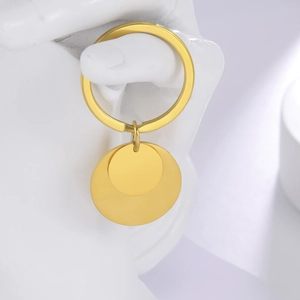 Macro detail of a gold stainless steel keychain with dual round tags on a white sculpture