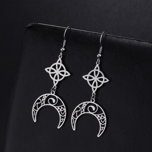 Detailed macro shot of silver Celtic knot and crescent moon earrings on black leather display