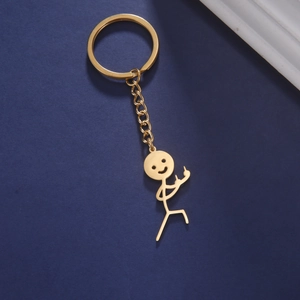 Macro detail of a gold-finish middle finger stickman keychain on a dark background