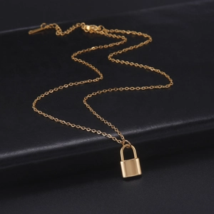 Detail view of gold padlock pendant on fine cross chain over textured black leather