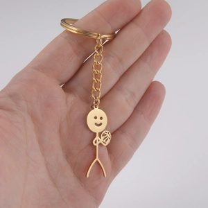 Golden stick figure keychain holding a ball with smiley face on a human hand