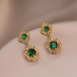 Detail of vintage gold earrings with emerald green crystals on champagne silk background