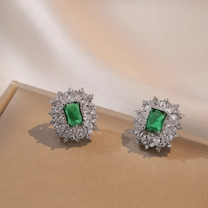 Boucles d'oreilles émeraude élégantes avec halo de diamants sur une boîte à bijoux dorée
