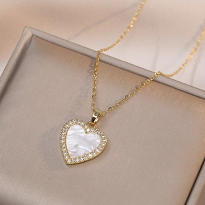 Collar de corazón dorado con nácar blanco y circonitas sobre una placa de champán