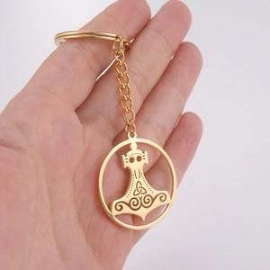 Golden keychain with Mjolnir hammer pendant and Celtic knots held by a person