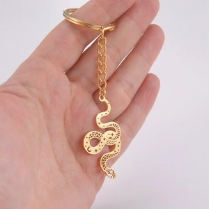 Golden stainless steel snake pendant keychain with hollow twisted design held in hand