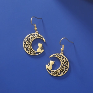 Detail of gold moon and cat silhouette earrings with intricate filigree on dark background