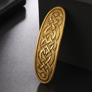 Detailed close-up of a vintage gold Celtic knot hair clip with intricate metallic patterns