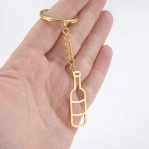 Golden stainless steel wine bottle keychain with hollow pendant held in hand on white background