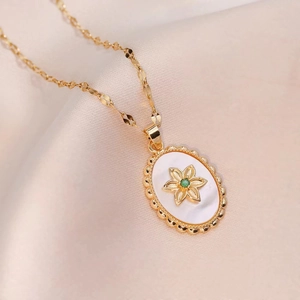 Goldene ovale Blumenkette mit weißem Muscheleinleger und grünem Stein auf weicher Seide