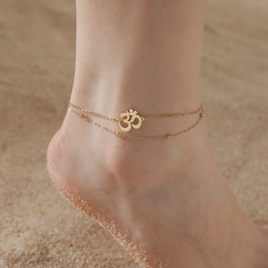 Double-layer gold stainless steel Om anklet with beads on a sandy beach setting