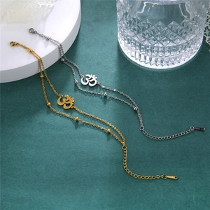 Detailed macro view of Om symbol charms on gold and silver stainless steel layered anklets