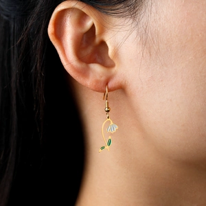 Vue détaillée d'une boucle d'oreille fleur dorée avec émail blanc sur le modèle