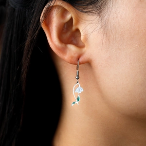 Détail des boucles d'oreilles muguet en émail blanc portées sur l'oreille d'un mannequin