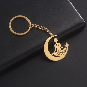 Détail de porte-clés doré en forme de lune de yoga sur fond en cuir noir texturé