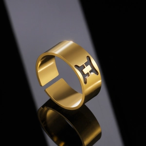 Macro detail of gold stainless steel Gemini constellation open ring on reflective surface