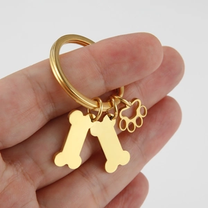 Porte-clés doré en acier inoxydable avec pendentifs os et patte tenu à la main