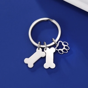 Porte-clés en acier inoxydable avec pendentifs en forme d'os et de patte sur fond bleu mat