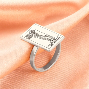 Macro shot of silver stainless steel Tarot Hermit ring IX on pink silk fabric background