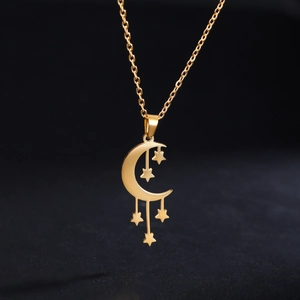 Detalle de un collar con colgante de media luna y estrellas doradas sobre fondo negro