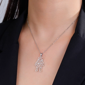 Close-up of a silver astronaut pendant necklace on a model wearing a black suit jacket